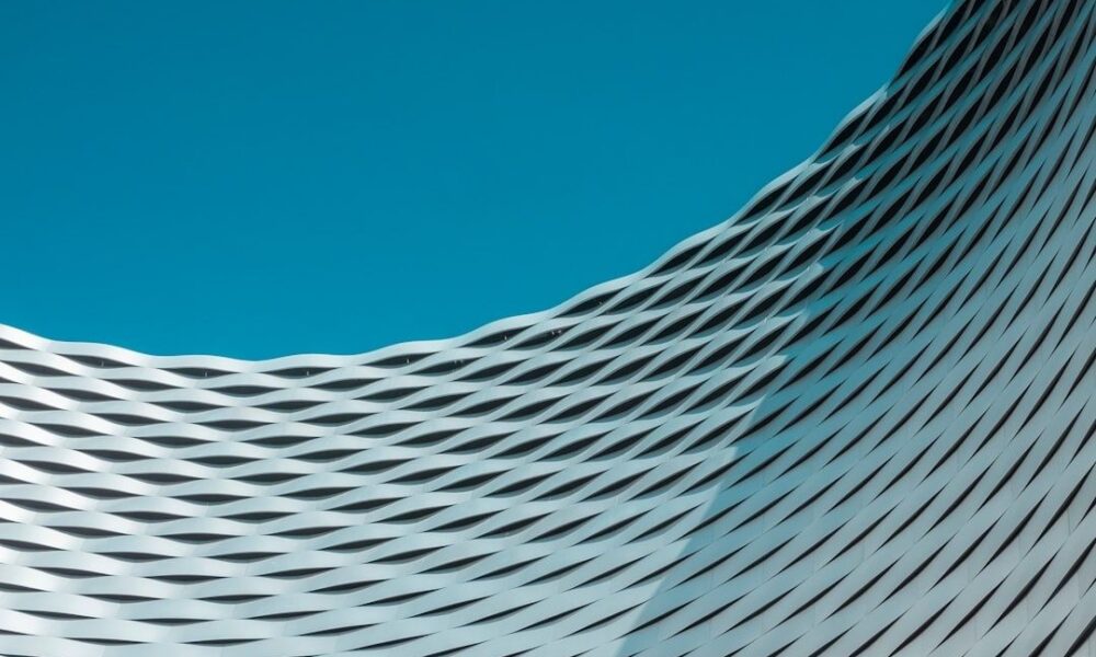 Abstrakte Fassade mit wellenförmigen Metalllamellen vor blauem Himmel