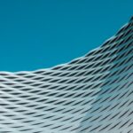 Abstrakte Fassade mit wellenförmigen Metalllamellen vor blauem Himmel