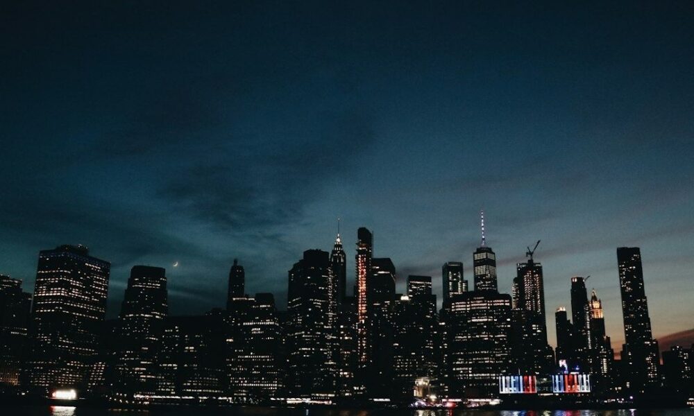Beleuchtete Skyline bei Dämmerung mit dunklem Wasser im Vordergrund